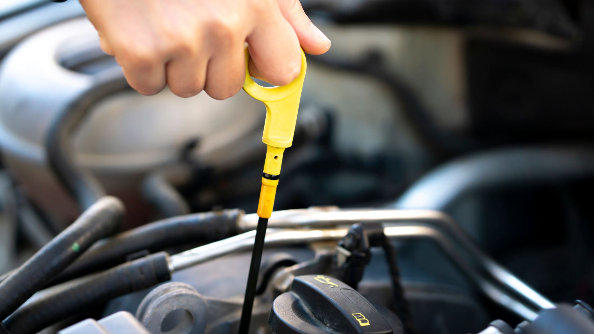 A person holding a yellow tool in front of a car engine